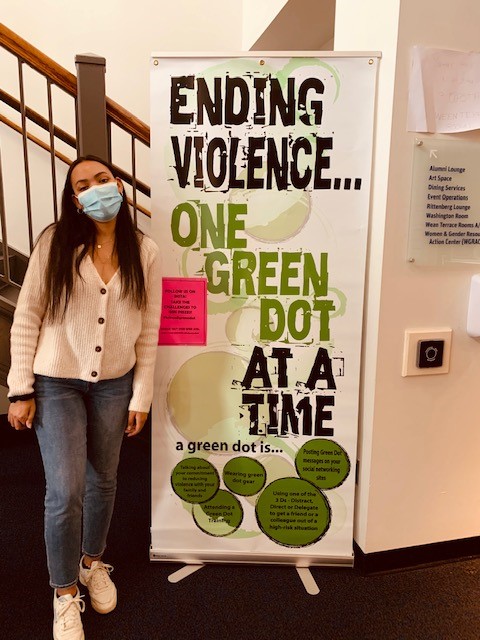 student standing near large green dot sign which reads, ending violence one green dot at a time